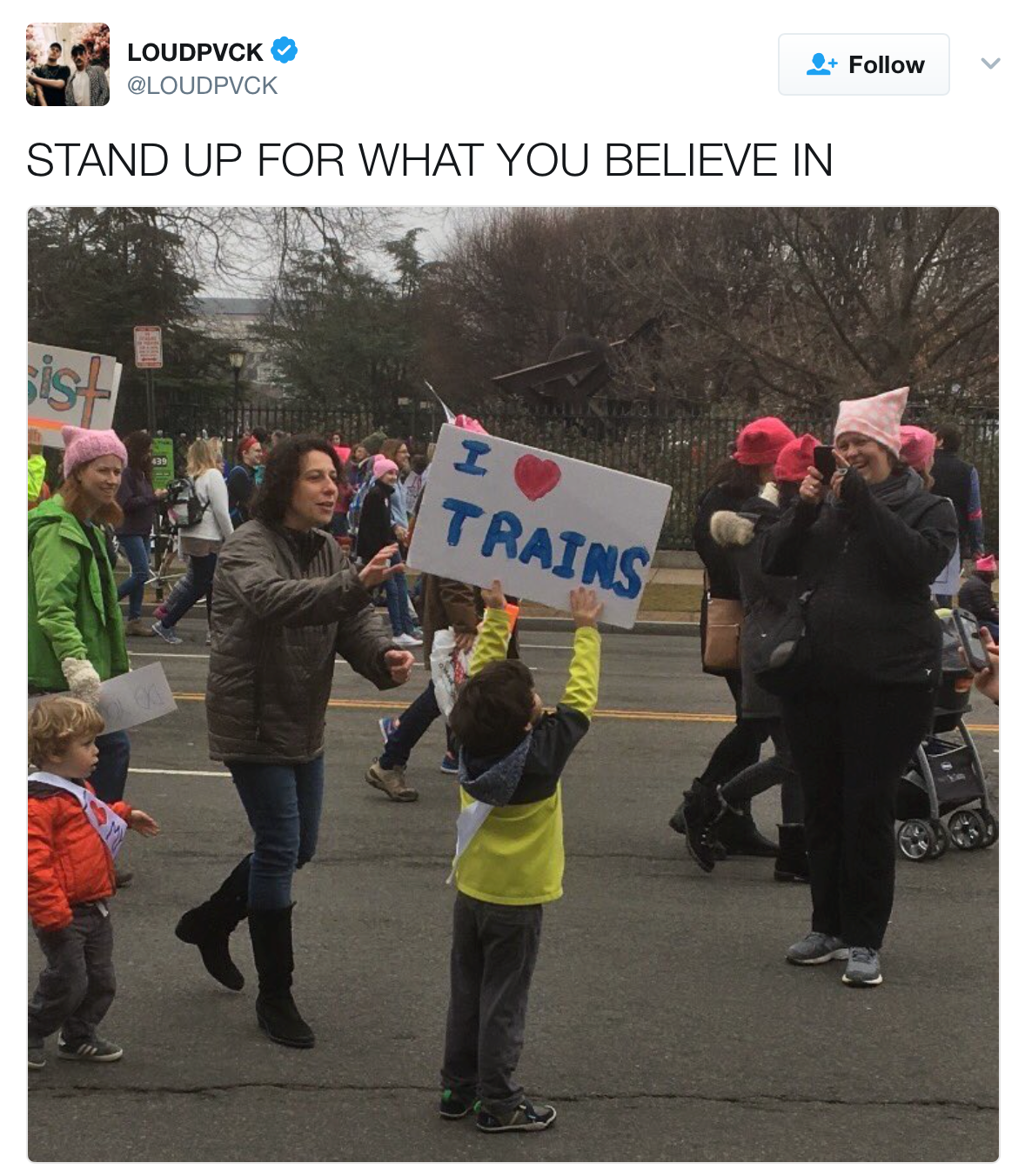 Tweet from LoudPVCK: 'Stand up for what you believe in'. Image: Amid a protest march in which many participants are wearing pink hats, a boy enthusiastically holds up a sign that reads 'I [heart] Trains.'